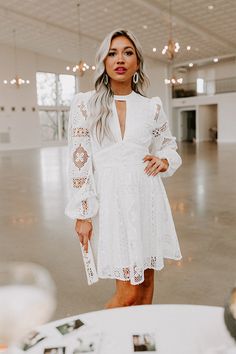 a woman standing in an empty room wearing a white dress with long sleeves and cut outs