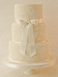 a three tiered wedding cake with white lace and bows on it's side