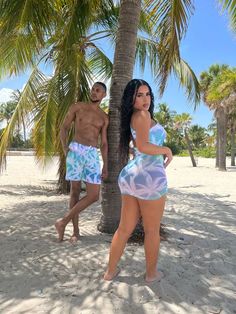 a man and woman in swimsuits standing under a palm tree on the beach