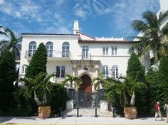 a large white house surrounded by trees and bushes with a gate in front of it