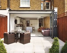 an outdoor living room and dining area with sliding glass doors on the outside wall, in front of a brick building