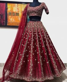 a red and gold bridal gown on display in front of a large piece of art