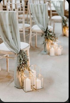 candles are lit in front of chairs with draping and greenery on them