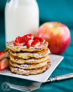 a stack of pancakes topped with strawberries and powdered sugar next to a bottle of milk