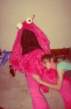 a young boy laying on the floor next to a large pink stuffed animal with eyes