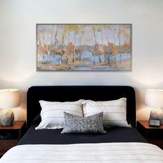 a bed with two lamps on each side and a painting hanging above the headboard