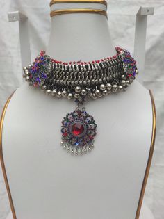 * This chunky kuchi Afghani necklace is embellished with multicolour glass stones, metallic weaving technique, and a dangling floral shaped pendant. The handmade craft is flaunting all the traditional vibes, along with a rusty silver tone. You can pair this exclusive piece with any traditional attire, as well as it would get along with any of your trendy outfits to add a pinch ethnic touch into your fashion statement. Note: The product is handmade, so slight change might occur in the actual prod Silver Jeweled Necklace For Festivals, Bohemian Jeweled Necklace For Celebration, Metal Jeweled Necklace For Festivals, Multicolor Metal Choker For Festivals, Bohemian Heavy Multicolor Necklaces, Heavy Bohemian Multicolor Necklaces, Heavy Multicolor Metal Necklaces, Bohemian Multicolor Necklaces, Heavy Multicolor Metal Necklace