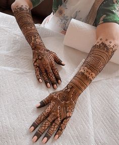 a woman with henna tattoos on her arm and hand is sitting on a bed