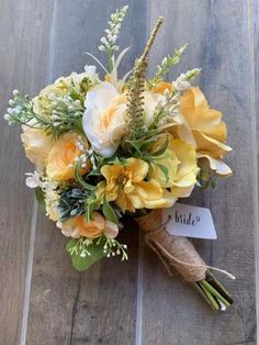 a bridal bouquet with yellow and white flowers on a wooden floor, the bride's name tag is attached to it