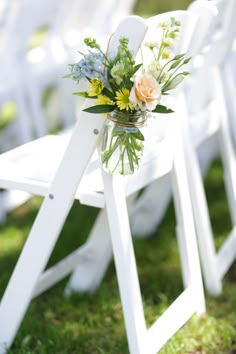 an arrangement of flowers in a mason jar on a white folding chair at a wedding ceremony