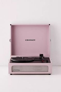 a pink record player sitting on top of a white table with the word crosley printed on it