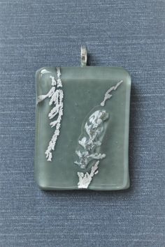 a square glass pendant with leaves on it