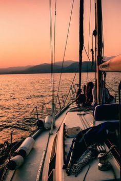 people are sitting on the deck of a sailboat at sunset