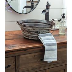 a large metal bowl sitting on top of a wooden counter next to a mirror and soap dispenser