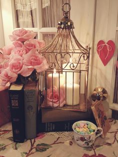 a table topped with pink roses next to a birdcage filled with candles and books