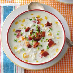 a bowl of soup with bacon, corn and cheese on the side next to a spoon