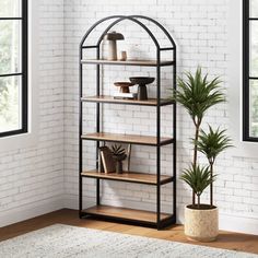 a book shelf with plants and books on it in front of a white brick wall