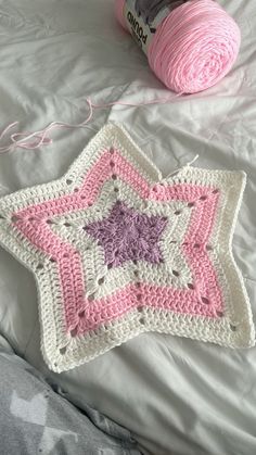 a pink and white crocheted star on top of a bed next to a ball of yarn