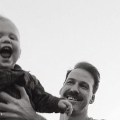 a man holding a baby up to his face and smiling at the camera while another person holds him