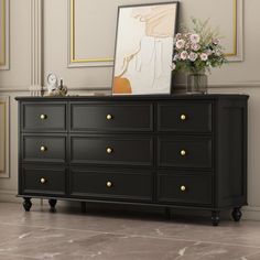 a black dresser with flowers on top and a mirror above the drawers in an empty room