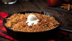 a skillet filled with food sitting on top of a wooden table next to an apple