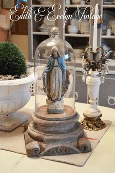 a statue under a glass dome sitting on top of a table next to a potted plant