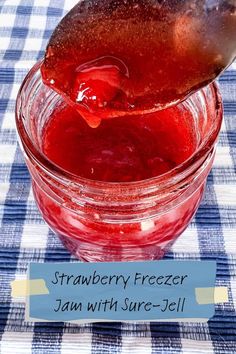 strawberry freezer jam with sure - jel in a glass jar on a checkered tablecloth