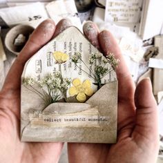 a person holding up a small house shaped card with flowers on it's front