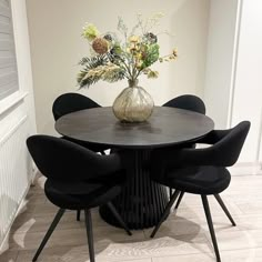 a round table with black chairs around it and a vase filled with flowers on top