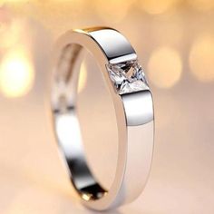 a white gold ring with a princess cut diamond set in the center, on a shiny background