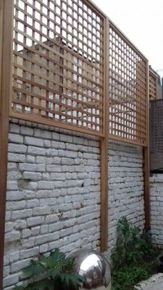 a white brick wall with a wooden trellis on the top and bottom part, next to a metal ball