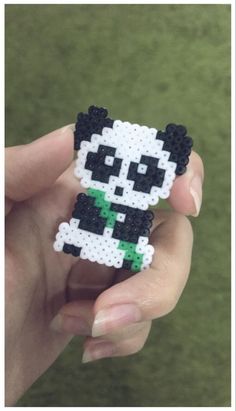 a person holding a small pixelated panda bear in their left hand and wearing a green shirt