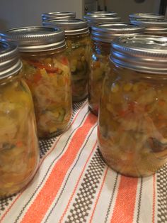 several jars filled with pickled vegetables on top of a striped table cloth next to a refrigerator