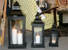 three lit candles sitting on top of a chair in front of a yellow and white wall