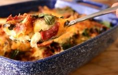 a spoon full of food in a blue dish on a wooden table with a person holding it