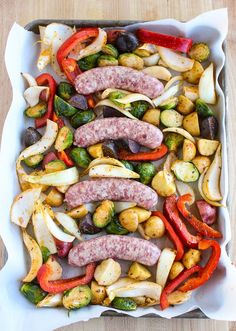 sausages, potatoes and peppers in a baking dish on a wooden table with utensils