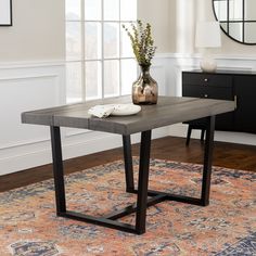 a table with a vase on top of it in front of a rug and window