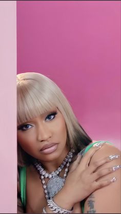 a woman with long blonde hair and blue eyes posing for a photo in front of a pink wall