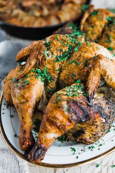 a whole chicken on a white plate with parsley sprinkled around it's legs