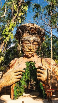 a large wooden statue sitting in the middle of a forest filled with trees and plants