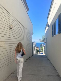 a woman is walking down an alley way with her hand on her hip and looking at the ocean