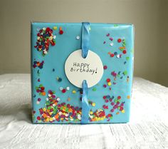 a blue gift box with confetti on it and a happy birthday tag attached