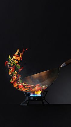 a wok with food being cooked on top of it and flames coming out from the bottom