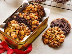 some cookies are sitting in a tin on a table next to a red ribbon and two chocolate covered cookies