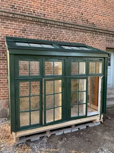 a small green building sitting in front of a brick wall with windows on the side