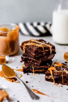 three chocolate brownies with caramel drizzle on top and two spoons next to them