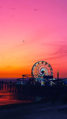 a ferris wheel sitting on top of a pier next to the ocean at night time