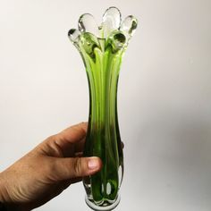 a hand holding a green glass vase with flowers in it's center and bottom