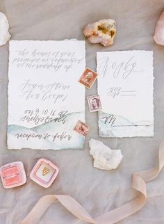 the wedding stationery is laid out with stamps and ribbons