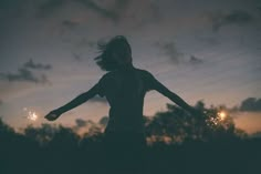 a girl is holding her arms out as the sun sets in the sky behind her